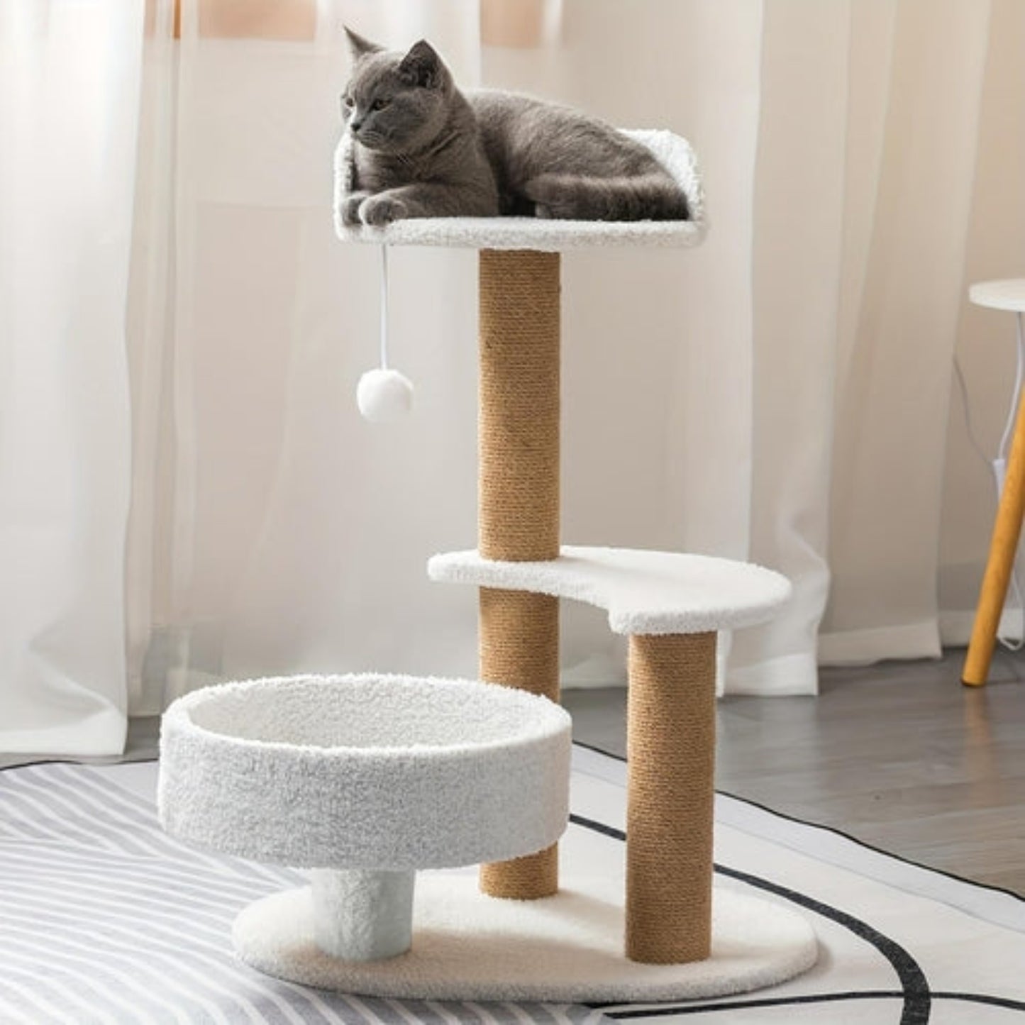 Cat sitting on a multi-level cat tree with white cushioned platforms and brown sisal-covered post.