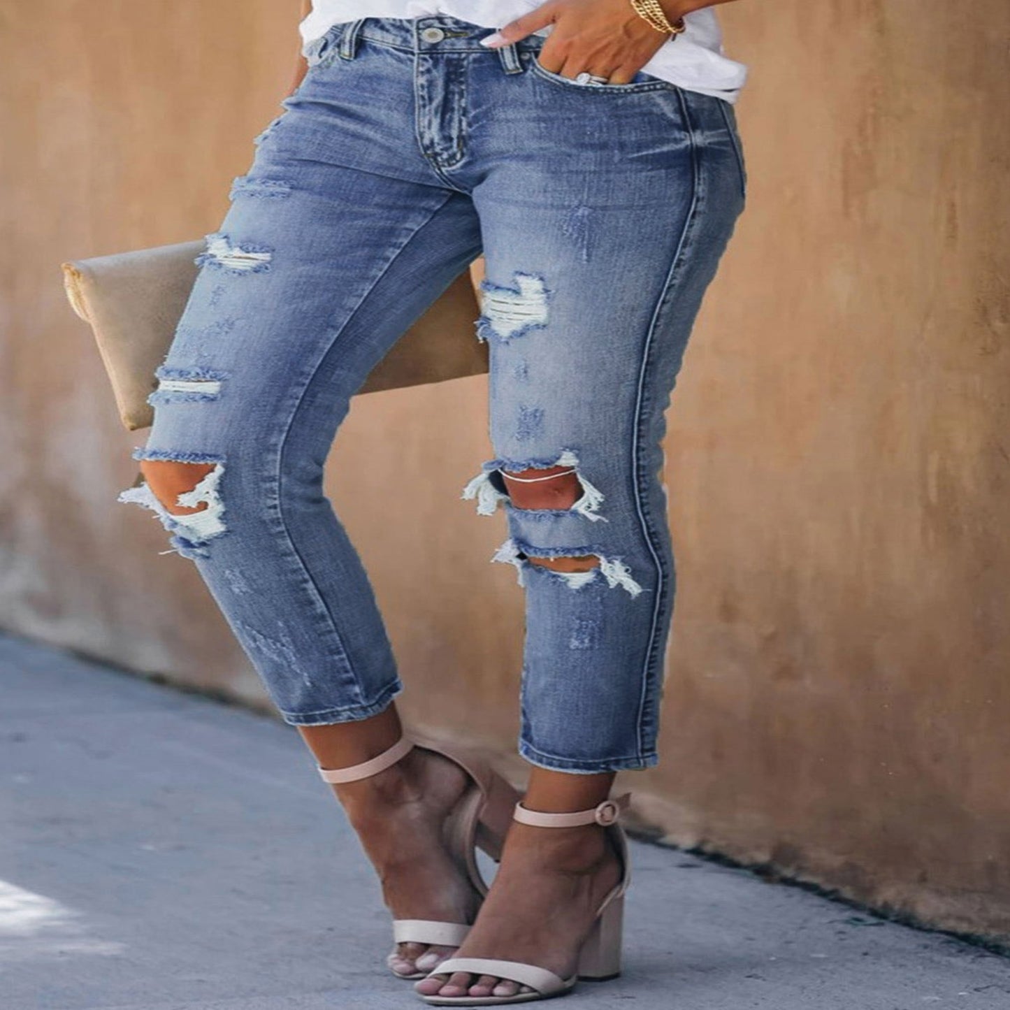 Ripped blue jeans worn by a person against a beige wall.