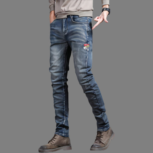 Person wearing blue jeans with a patch, standing against a gray background.