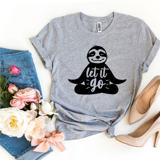 Gray t-shirt with sloth graphic and 'let it go' text, placed on a white surface with flowers and shoes.